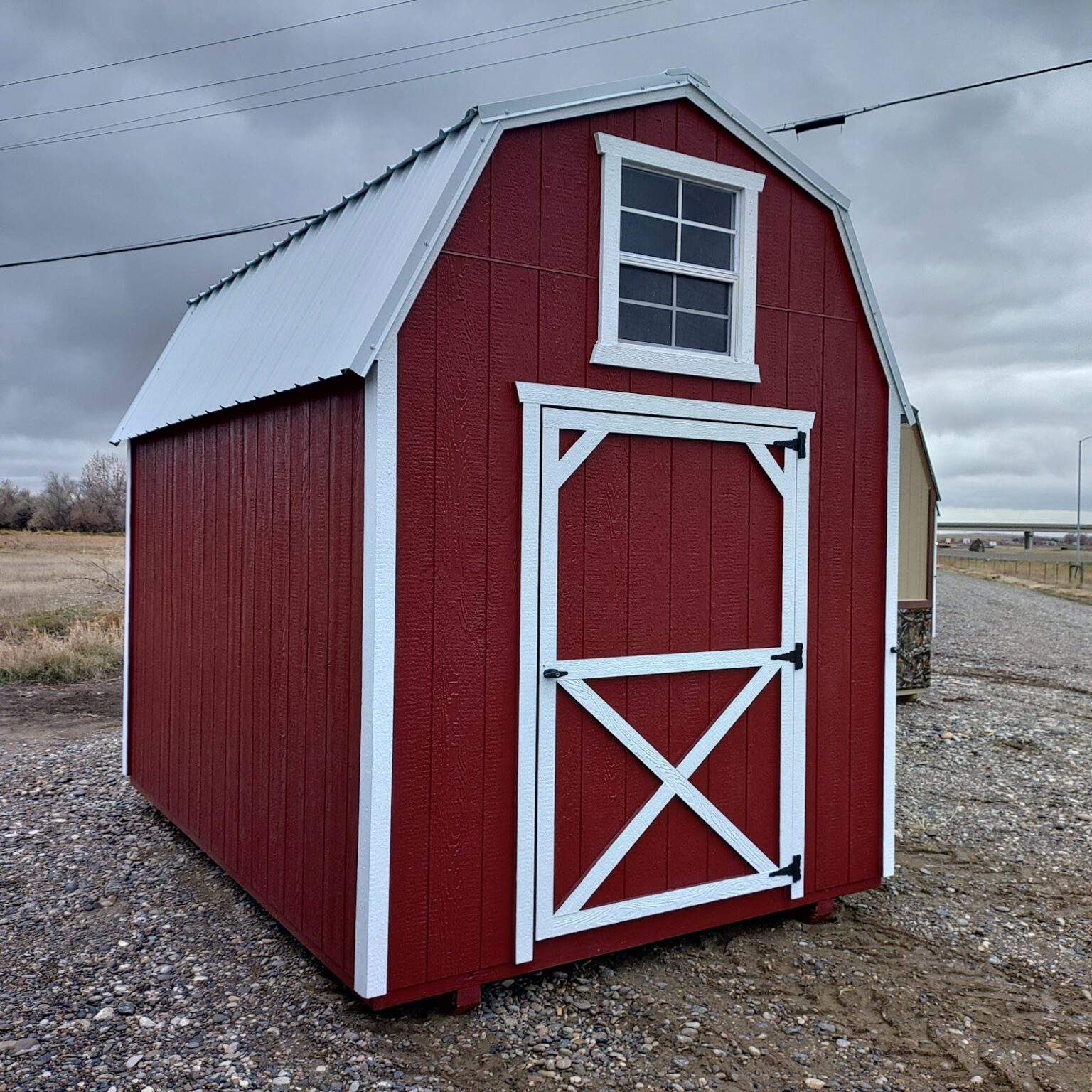 A cheery red and white 8x12 barn with a window in the gable and a barn door beneath.