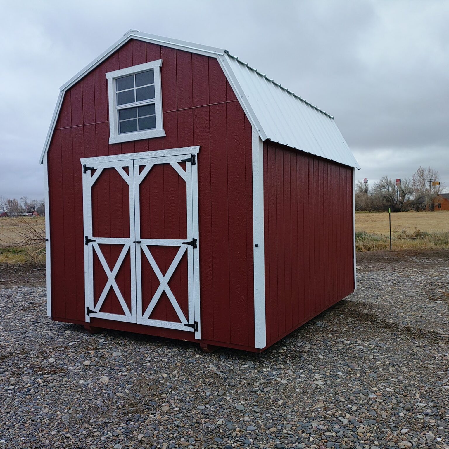 A charming red and white 10x12 barn with a window in the gable and double barn doors beneath the window.