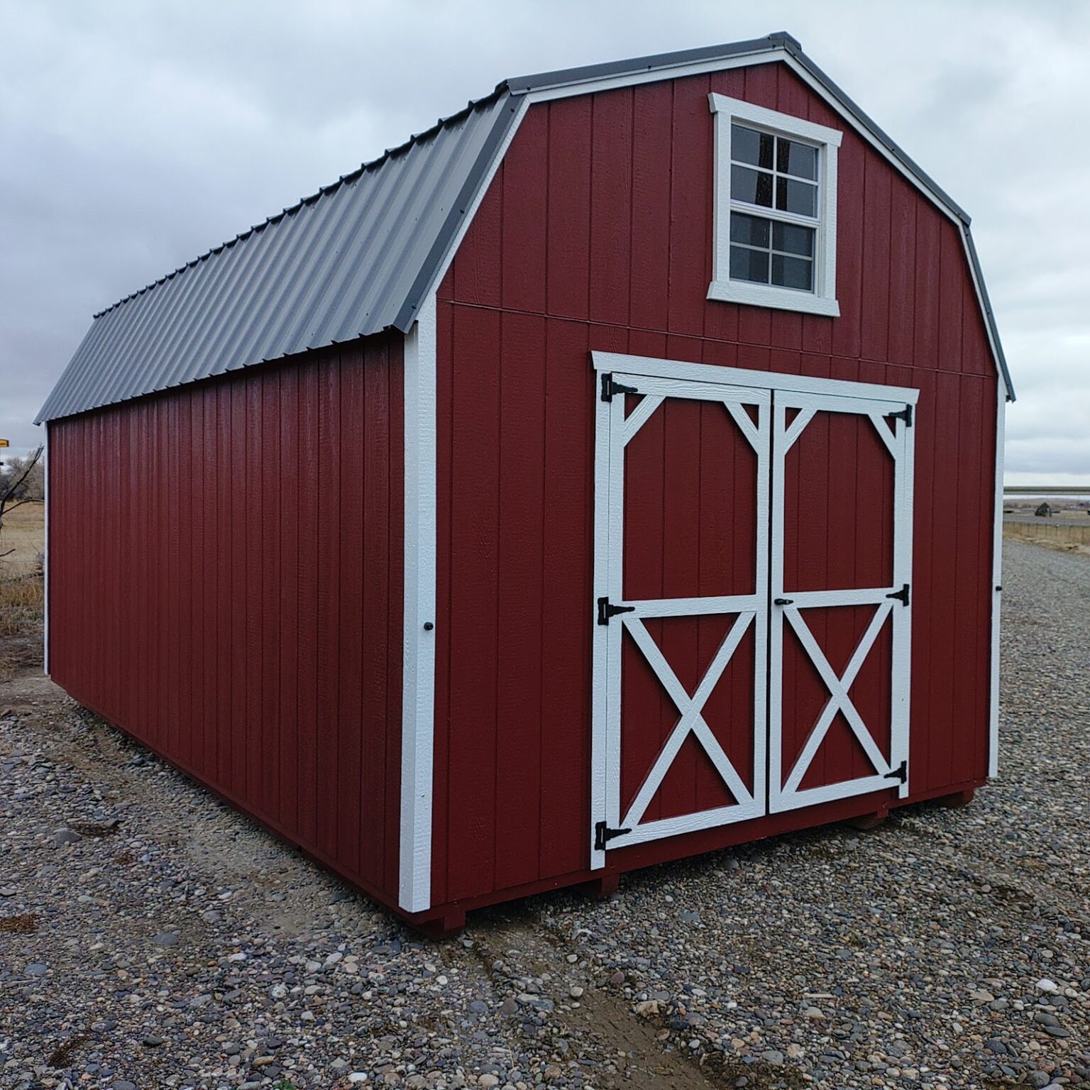 A stunning red and white 12x20 barn with a grey roof, a window in the gable and double barn doors beneath the window.